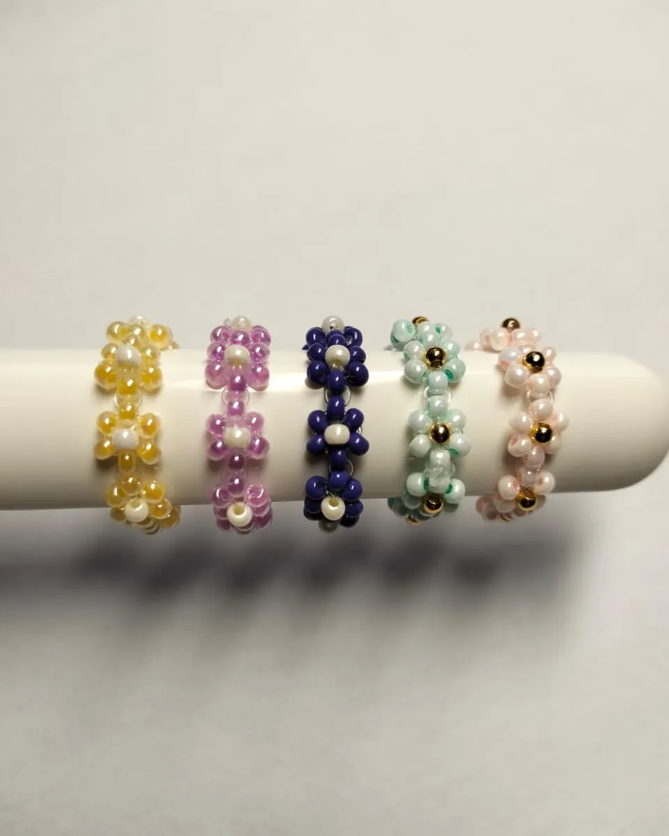 Five beaded daisy rings in yellow, lilac, navy, mint and blush on a white stand